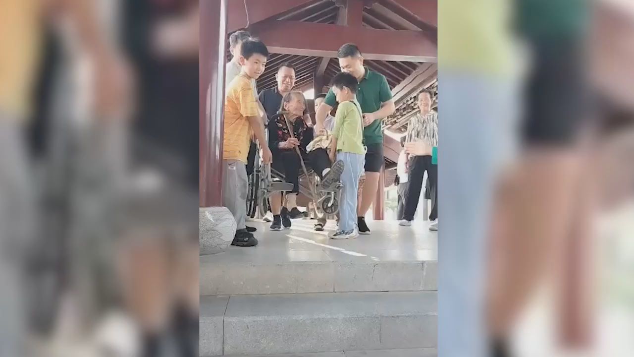 家人带96岁老人坐轮椅旅游，孙子、重孙7人抬她下台阶